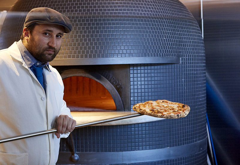 Chef and master pizzaiolo Daniele Udit removing a pizza from a wood burning oven