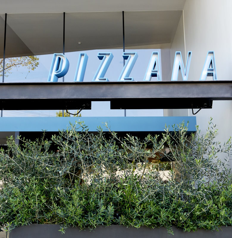 Facade of Pizzana Brentwood with bold blue signage set against a modern building with a red stripe