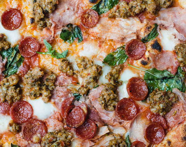 Closeup of Carnivoro pizza with pepperoni, sausage, prosciutto and basil
