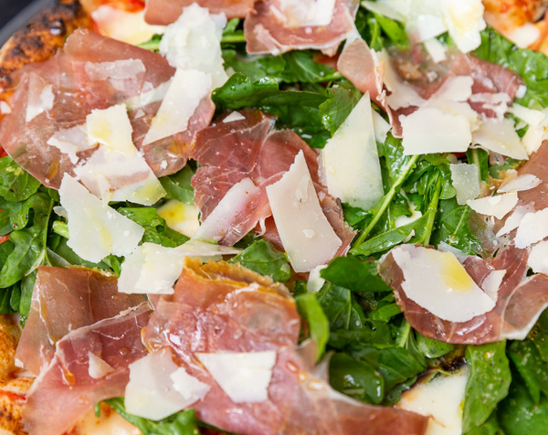 Closeup of Margherita al Crudo pizza with prosciutto, arugula and parmigiano