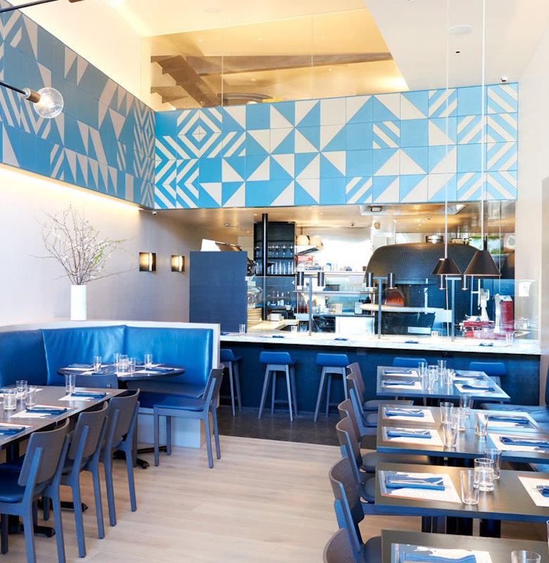Interior of Pizzana Brentwood featuring a cozy dining area with blue banquettes and a geometric patterned wall