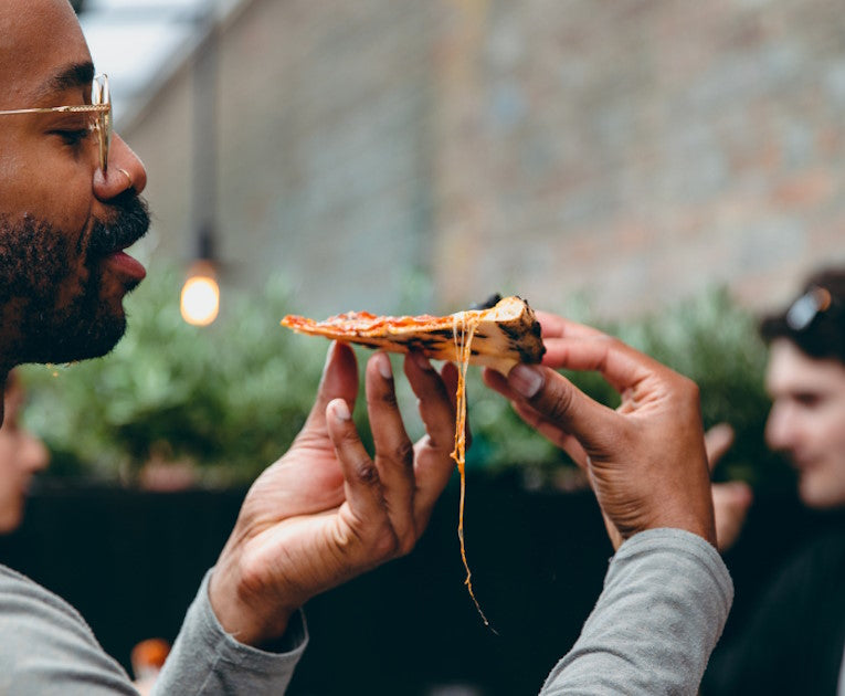 A man enjoying a hot, cheesy slice of pizza on Pizzana West Hollywood’s patio
