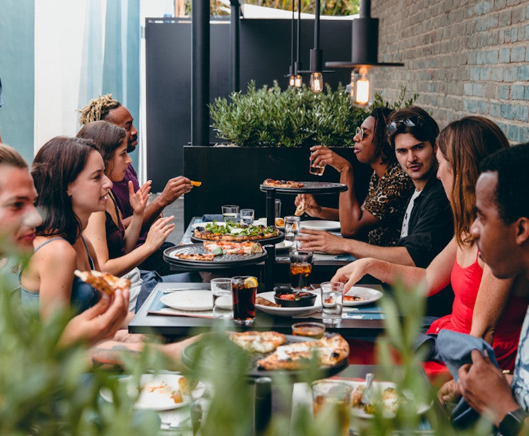 A lively outdoor dining scene on Pizzana West Hollywood’s outdoor patio with guests enjoying Neapolitan pizzas