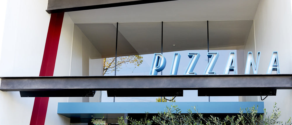 Facade of Pizzana Brentwood with bold blue signage set against a modern building with a red stripe