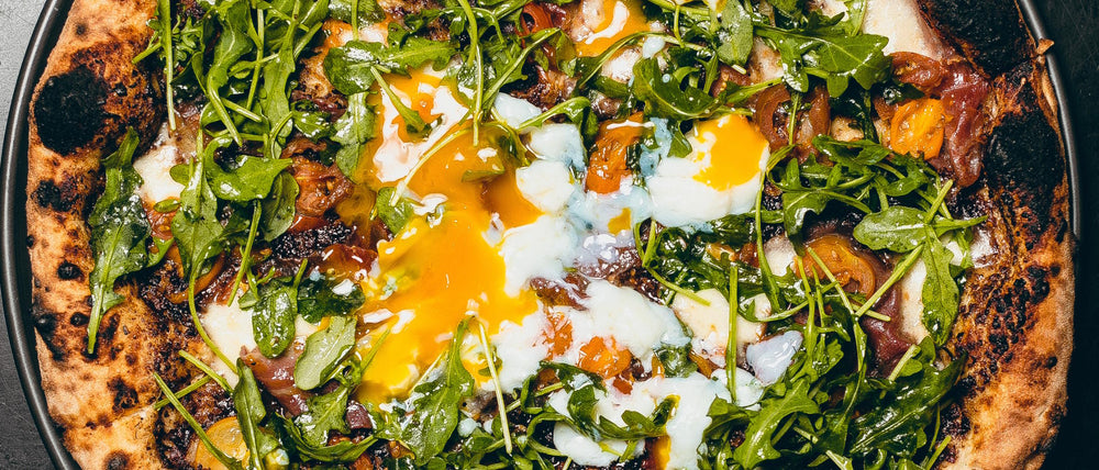 Uovo pizza featuring fior di latte, cherry tomato, prosciutto di parma, bacon jam, arugula and egg.
