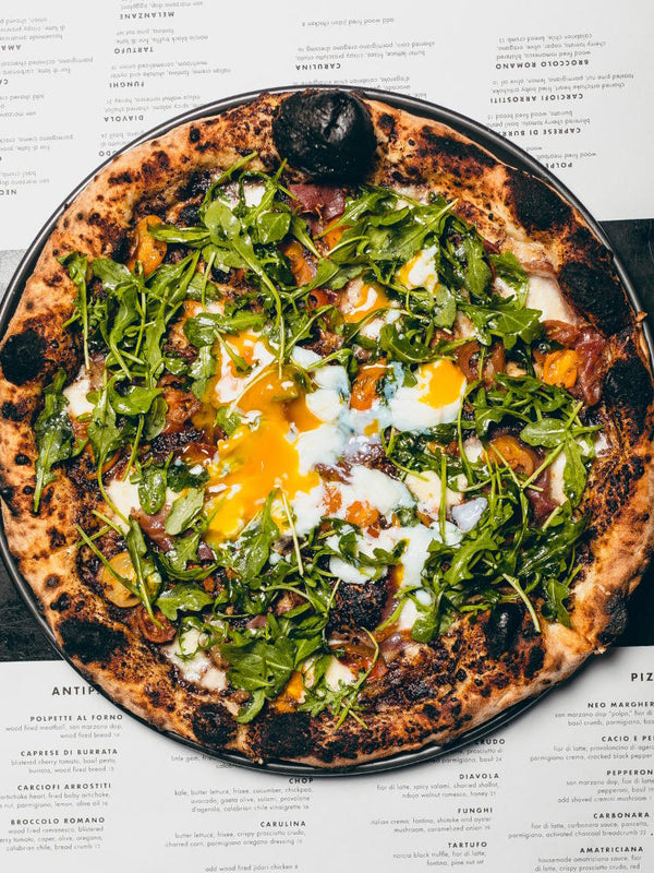 Uovo pizza featuring fior di latte, cherry tomato, prosciutto di parma, bacon jam, arugula and egg.