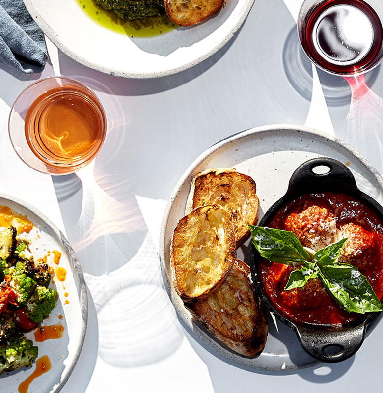 Overhead shot of Italian antipasti including meatballs and broccoli alongside a glass of wine