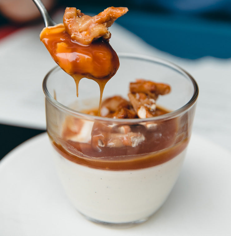 A spoon scooping out a bite of Panna Cotta with caramel sauce and pretzel