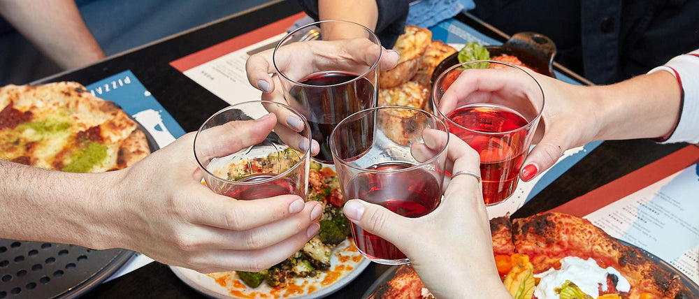 Four hands clinking wine glasses over a delicious spread of Italian pizzas and antipasti
