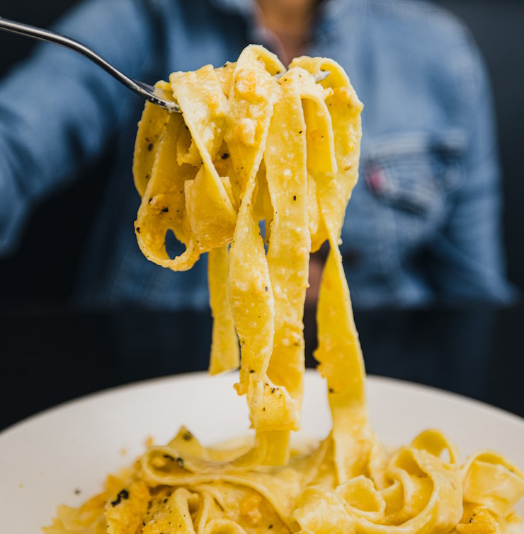 A fork holding up a large bite of cheesy Fetuccine pasta 