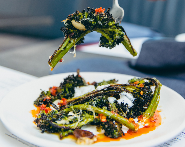 Fork lifting piece of wood fired Broccolini over plate 