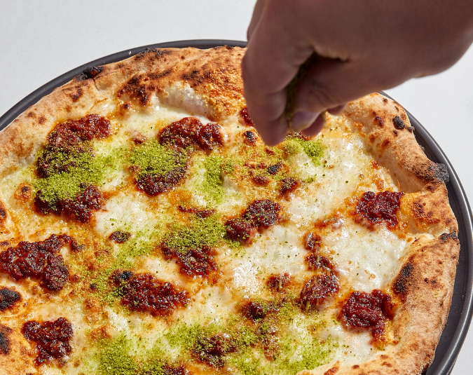 Hand sprinkling basil breadcrumb over Neo Margherita pizza